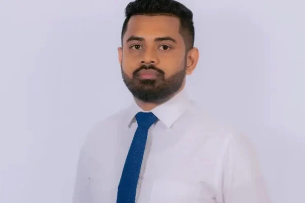 A man with short dark hair and a beard is wearing a white shirt and blue tie, standing against a plain light background, conveying professionalism. Punch Card
